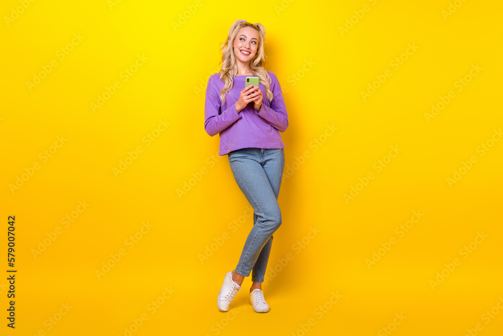 Full length photo of sweet dreamy woman wear violet shirt texting instagram twitter emtpy space isolated yellow color background Full length photo of sweet dreamy woman wear violet shirt texting instagram twitter emtpy space isolated yellow color background
