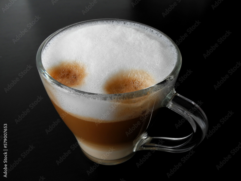 Frothy hot latte made by coffee machine in glass cup on black table surface close-up Frothy hot latte made by coffee machine in glass cup on black table surface close-up