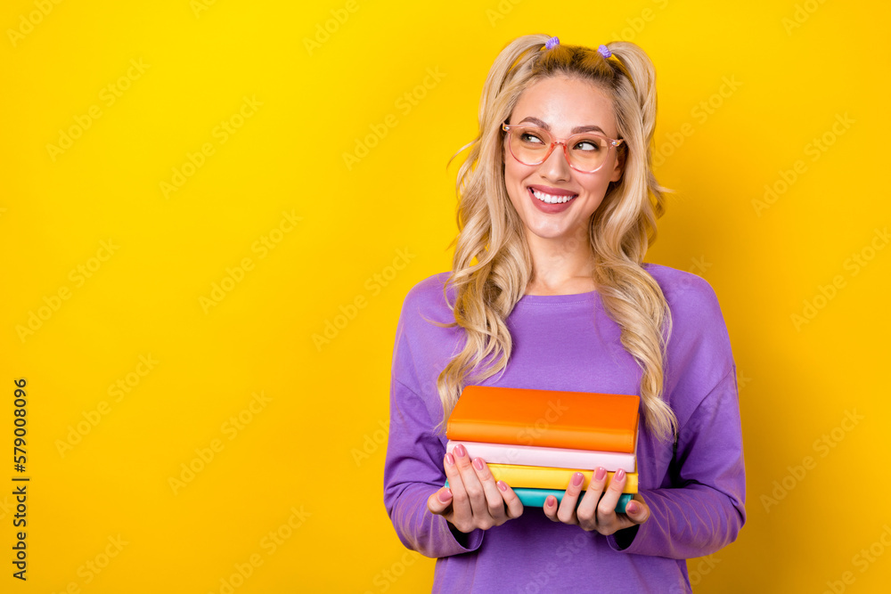 Photo of positive dreamy woman wear violet shirt holding book stack pile looking emtpy space isolated yellow color background Photo of positive dreamy woman wear violet shirt holding book stack pile looking emtpy space isolated yellow color background
