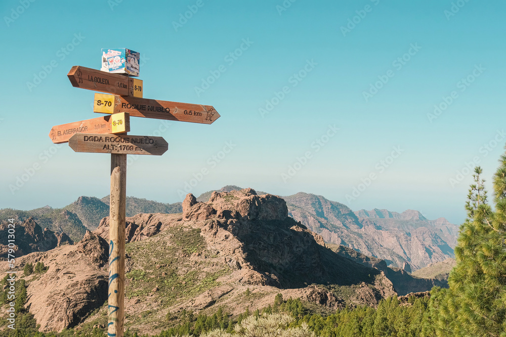 A wooden signage for travellers on a wild volcanic landscape with pine trees, cliffs and rock formations in Pico de las Nieves, Tejeda, Gran Canaria. Clear and sunny day