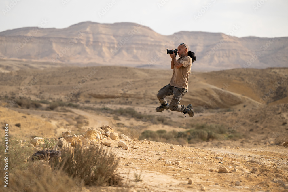 A photographer is jumping and taking a photo while in the air, outside in the Negev desert in Israel.