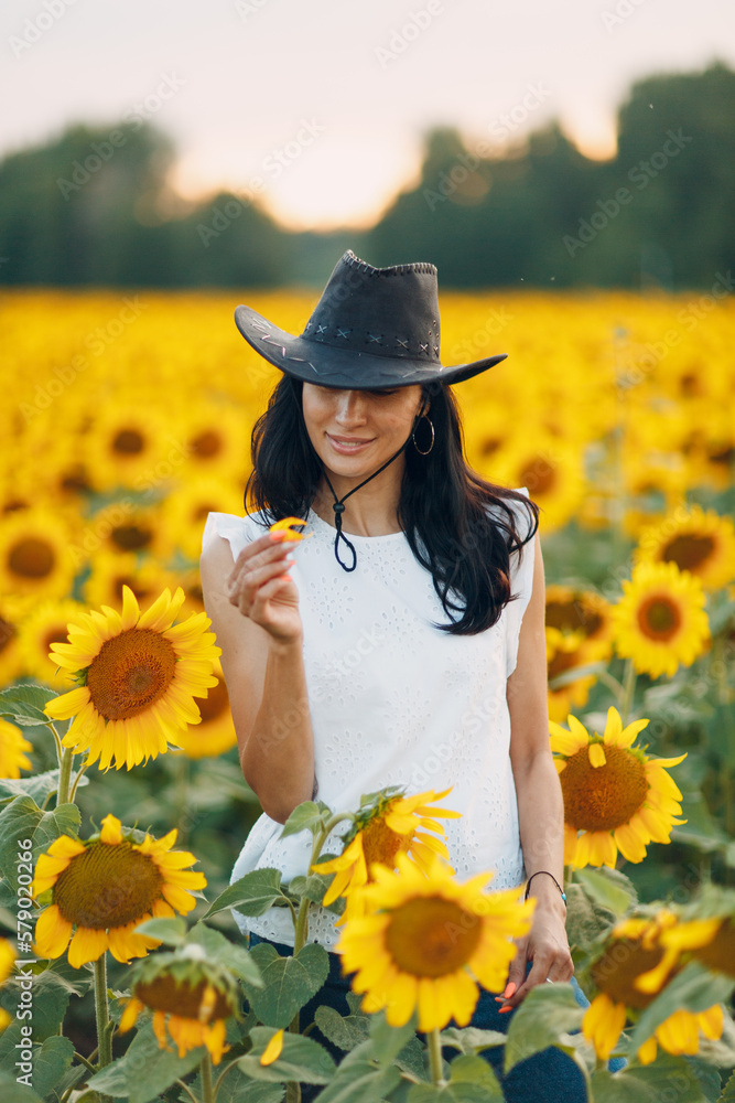 Beautiful young woman in hat on sunflower field.