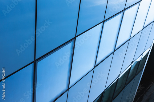 The blue sky is reflected in the windows of a modern office building. Architecture and exterior of contemporary houses