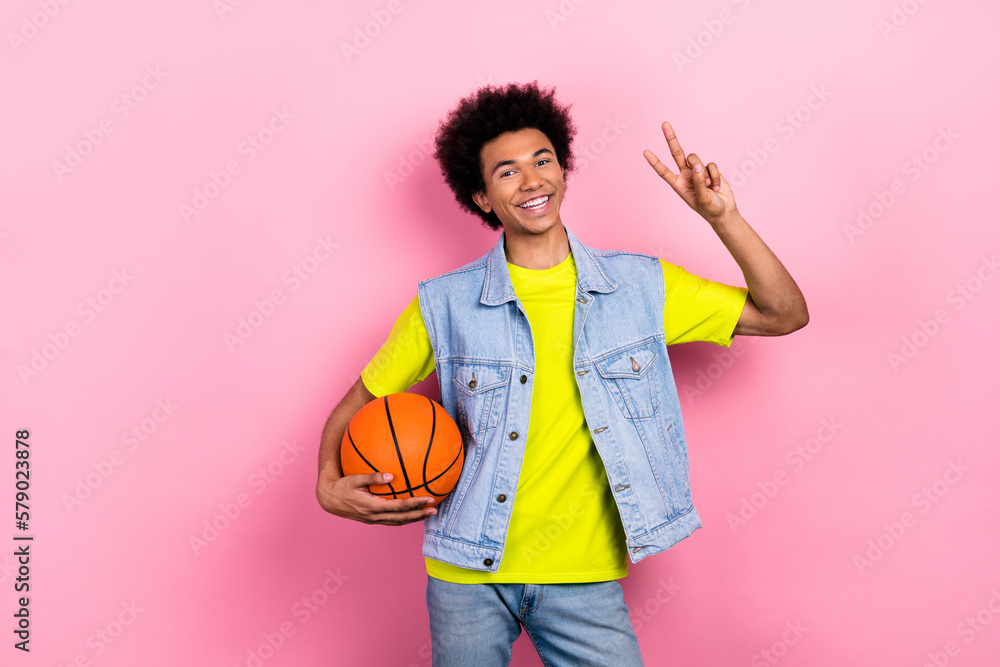 Portrait of positive person hold basketball hand fingers demonstrate v-sign isolated on pink color background