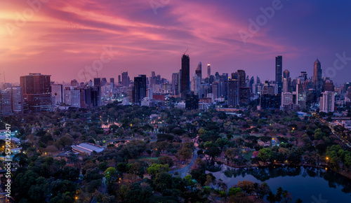 Elevated, panoramic view over the popular Lumphini Park to the illuminated, modern city skyline of Bangkok, Thailand, during a colorful dusk