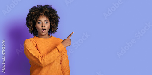 Amazed black woman pointing at copy space and grimacing