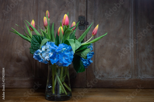 bouquet tulipes et hortensia vase transparent devant portes anciennes Fototapet
