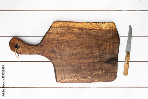 Empty wooden cutting board and rustic knife placed on white wood planked table with copy space