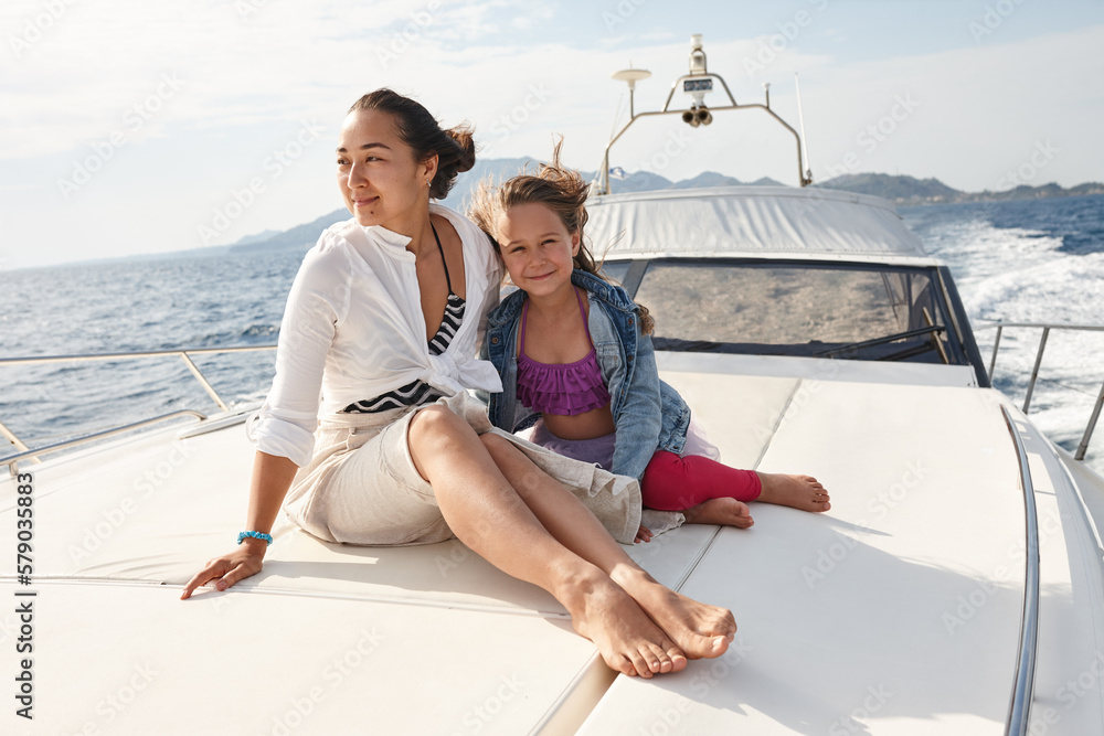 Happy mother and daughter on white yacht in the sea during summer vacation