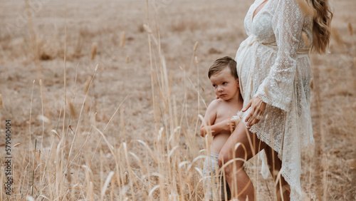 Mother pregnant with second child standing with son in brown grass outside photo