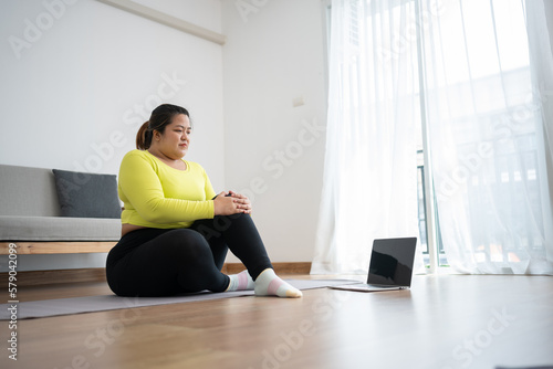 Asian overweight woman doing stretching exercise at home on fitness mat. Home activity training, online fitness class. Stretching training workout on yoga mat at home for good health and body shape.