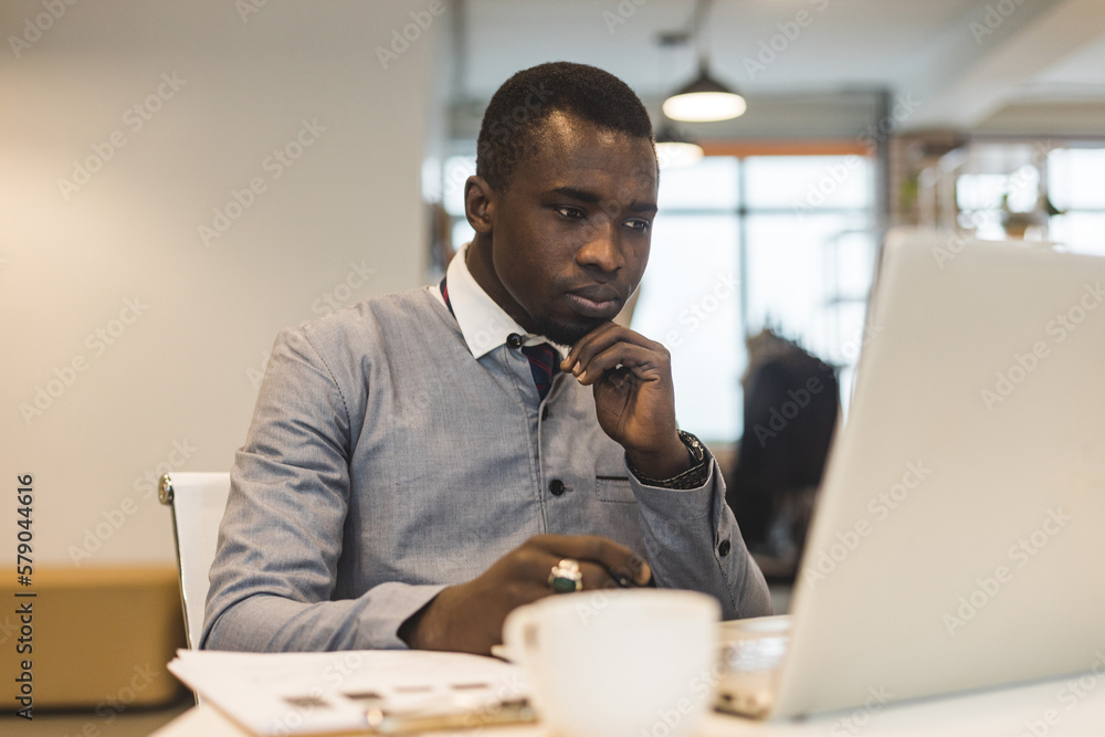 Obraz premium Portrait of an African American in the office. Black man in a business suit working on a laptop