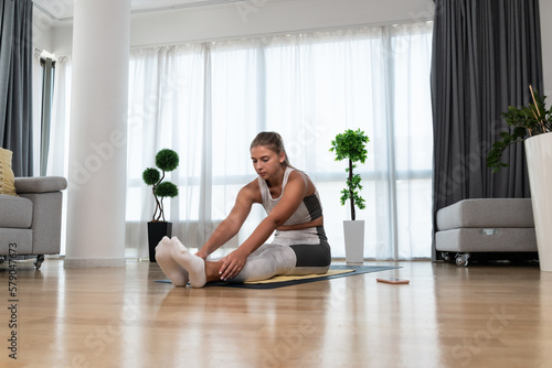 Strong sweaty and beautiful athletic fitness girl in sportswear doing exercises and home workout in her bright and spacious living room with minimalist interior. Self love confident woman practice