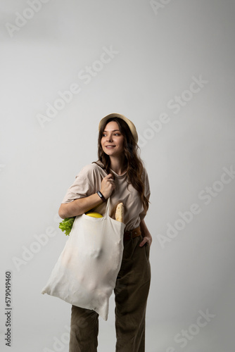 Zero waste concept. Young brunette woman holding mesh eco bag with organic fruits and vegetables. Using reusable crochet net bag for grocery shopping.