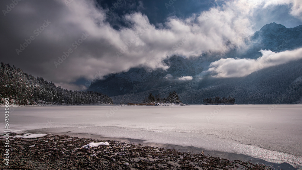 Alpin winter lake with snowy cover morning sun clouds fir and mountains