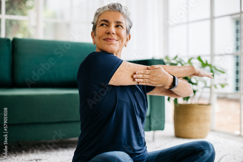 Fototapet Happy and healthy senior woman doing a cross arm stretch in a peaceful yoga sess