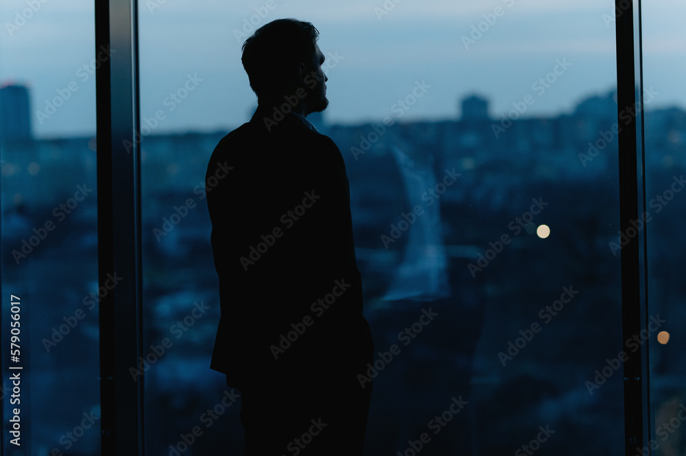 Silhouette of a Business Man looking out of high rise office window at night. a man in a classic suit near a window Silhouette of a Business Man looking out of high rise office window at night. a man in a classic suit near a window