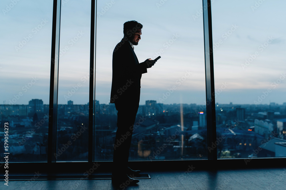 Silhouette of a business man with a mobile phone near the office window at night Silhouette of a business man with a mobile phone near the office window at night