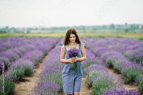 Fototapeta Naklejka Na Ścianę i Meble -  Beautiful girl hold bouquet purple lavender flowers in field. Female collect lavender. Woman in the lavender field. Enjoy the floral glade, summer. Down view. Close up