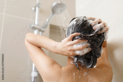 Woman taking shower and washing hair with shampoo in bathroom at home