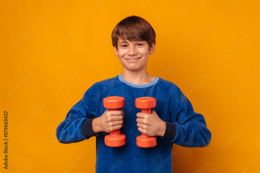 Smiling teen boy is holding two orange dumbbells in front of his chest. Smiling teen boy is holding two orange dumbbells in front of his chest.