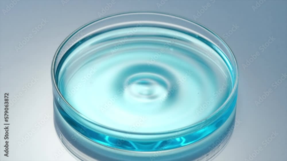 Close up scene of water drop dropping on surface of blue liquid on petri dish, create small waves and bubbles in slow motion. Concept of medicine or cosmetic research and organic skin or body care pro Close up scene of water drop dropping on surface of blue liquid on petri dish, create small waves and bubbles in slow motion. Concept of medicine or cosmetic research and organic skin or body care pro