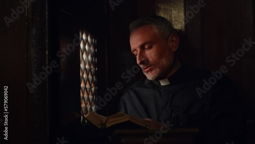 The priest listens to confession while sitting in the confessional. A pastor in a black robe is quoting a passage from the Bible to a man. photo