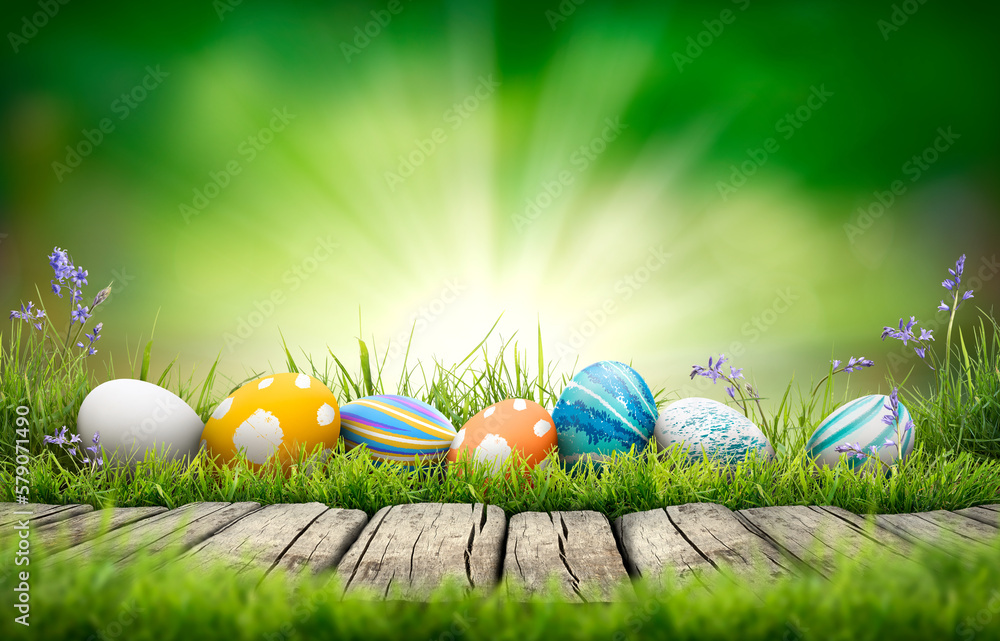 A collection of painted easter eggs celebrating a Happy Easter on a spring day with green grass meadow background with copy space and a rustic woodern bench to display products.