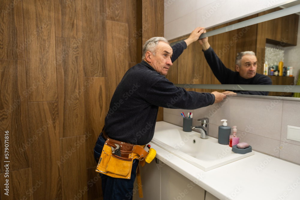 an elderly man repairs a bathroom mirror