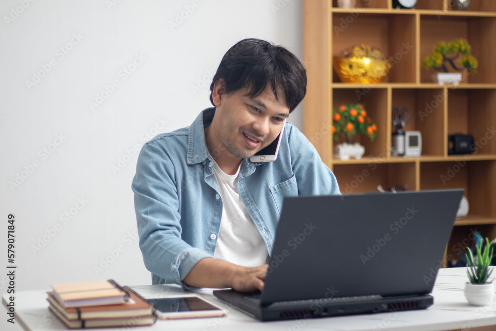 Man wearing jeans jacket talking on the phone sitting in front of laptop Man wearing jeans jacket talking on the phone sitting in front of laptop