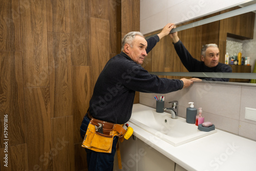 an elderly man repairs a bathroom mirror