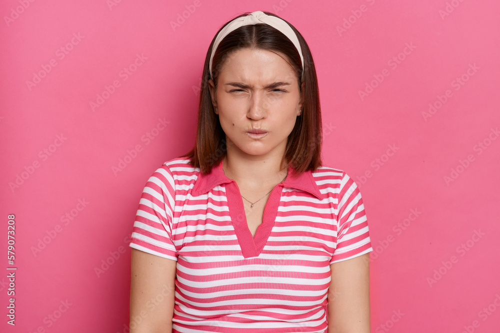Portrait of angry frustrated young girl with brown hair wearing striped casual t shirt standing isolated pink background, clenched teeth and closed eyes, arguing, expressing negative emotions and hate Portrait of angry frustrated young girl with brown hair wearing striped casual t shirt standing isolated pink background, clenched teeth and closed eyes, arguing, expressing negative emotions and hate