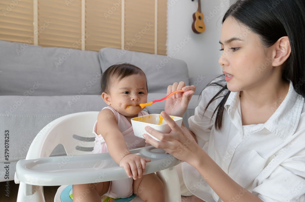 Young mother helping baby eating blend food on baby chair Young mother helping baby eating blend food on baby chair