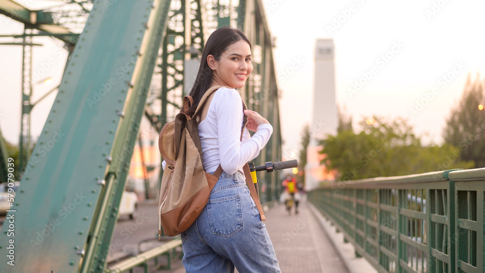 Portrait of young beautiful woman with an electric scooter  over bridge in modern city  background