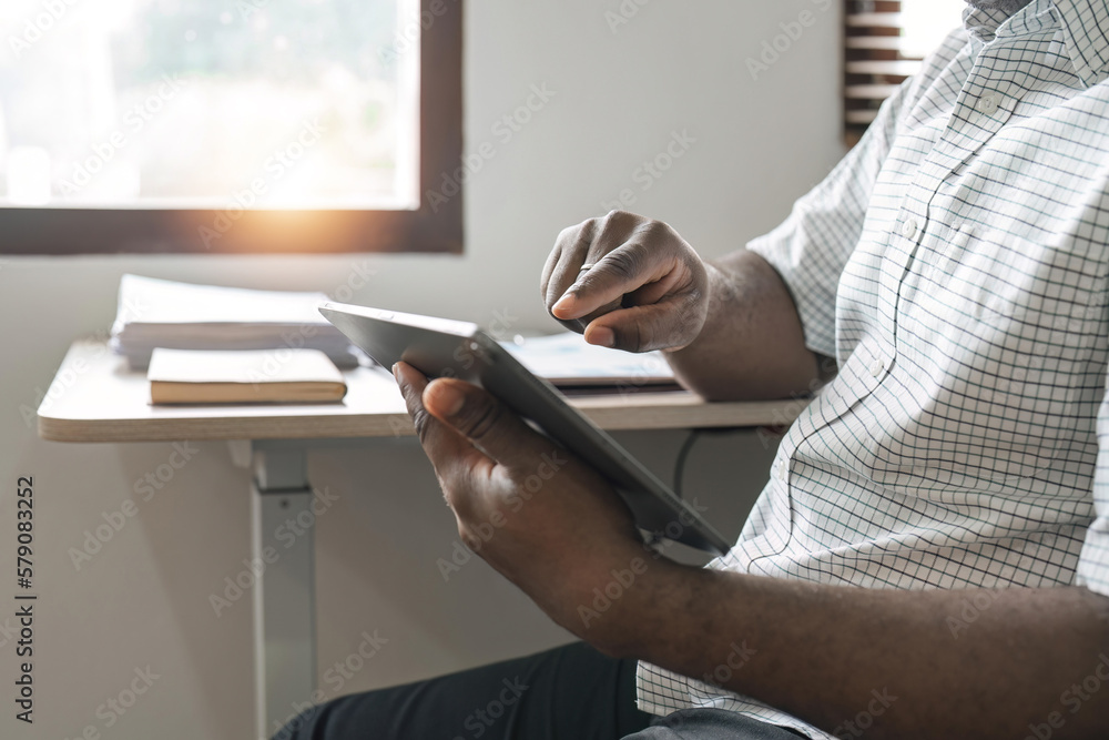 Fototapeta premium Smiling African American freelancer touching screen digital tablet while working in new project at home. Black businessman looking for information on Internet