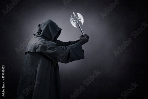 Figure in hooded cloak with axe over dark misty background