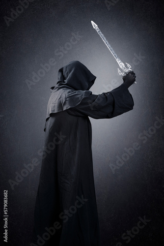 Dark knight with hooded cape and medieval sword over dark misty background photo