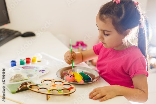 a little girl paints a toy fox made of clay. DIY concept.