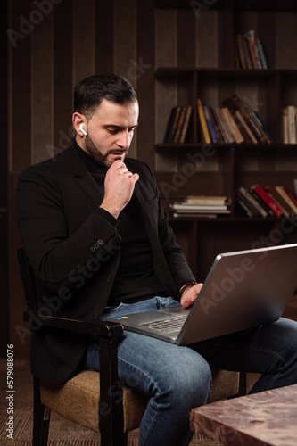 handsome bearded male bussiness man is wirking with a laptop in his home office photo