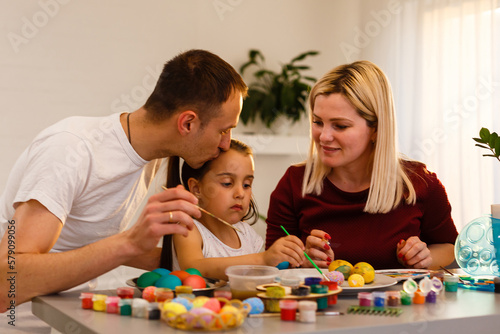 Happy family painting Easter eggs at table in kitchen.