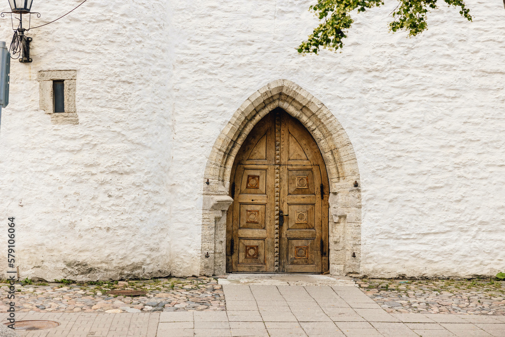 Ancient wooden arched doorway set into old white wall in medieval centre of European city