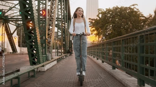 Portrait of young beautiful woman with an electric scooter  over bridge in modern city  background