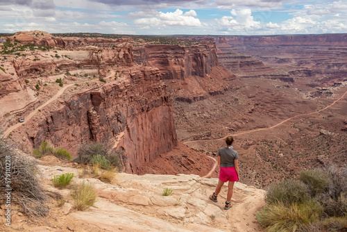 Woman with scenic view from Shafer Trail Viewpoint in Canyonlands National Park near Moab, Utah, USA. Shafer Basin and La Sal Mountains in Colorado Plateau. Off road trails leading down the canyon