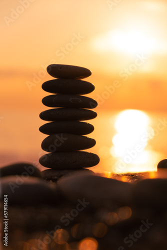 Vertical İmage, Balanced pebble pyramid silhouette on the beach at sunset. Zen stones on the sea beach, meditation, spa, harmony, calmness, balance concept. 