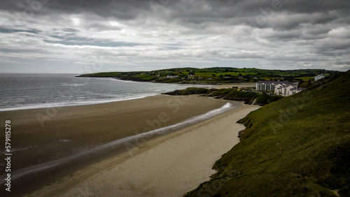 Picturesque southern Irish sandy beach of Inchydoney at low tide on a cloudy day, top view. The coastline of the island of Ireland. Beautiful green hills on the Atlantic Ocean. Gray clouds in the sky.