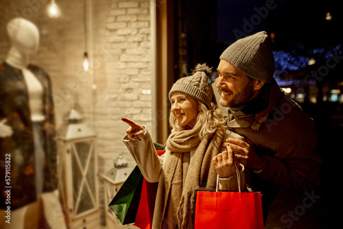 Happy couple with shopping bags looking at shop window in city