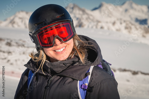 skier smiles in a safety ski helmet and goggles against the backdrop of the picturesque Alpine mountains. Active sports people and success concept image