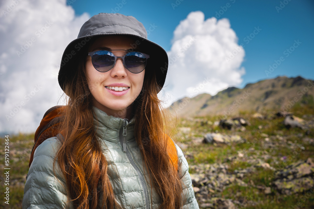 Portrait of a traveler in the mountains. The concept of adventure, travel and hiking. Happy woman in a cap enjoys the sunshine while hiking in the mountains. Tourist with glasses Portrait of a traveler in the mountains. The concept of adventure, travel and hiking. Happy woman in a cap enjoys the sunshine while hiking in the mountains. Tourist with glasses