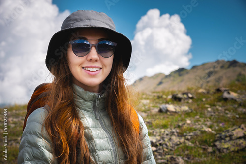 Portrait of a traveler in the mountains. The concept of adventure  travel and hiking. Happy woman in a cap enjoys the sunshine while hiking in the mountains. Tourist with glasses