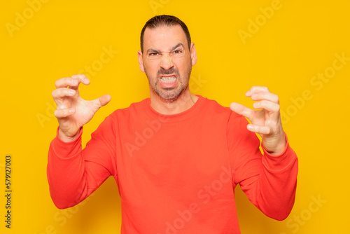 Bearded hispanic man in his 40s wearing a red jumper making claw gesture with an obvious angry, aggressive and thoughtful expression © Andres
